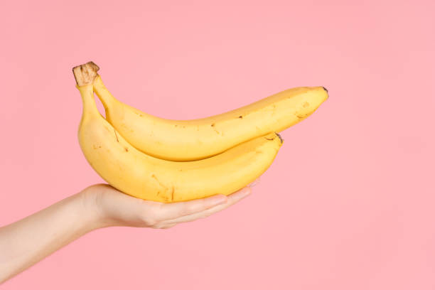 istock Yellow bananas in a woman's hand on a pink background 1347500193