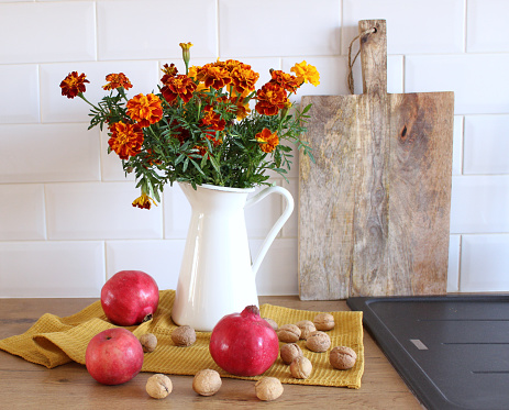 Closeup of Tagetes flowers, pomegranates and walnuts. Moody autumn bouquet.Selective focus. White brick wall.Modern Scandinavian design. Interior concept.