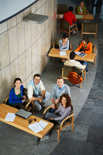 High angle view of smiling university students sittings at tables in hallway