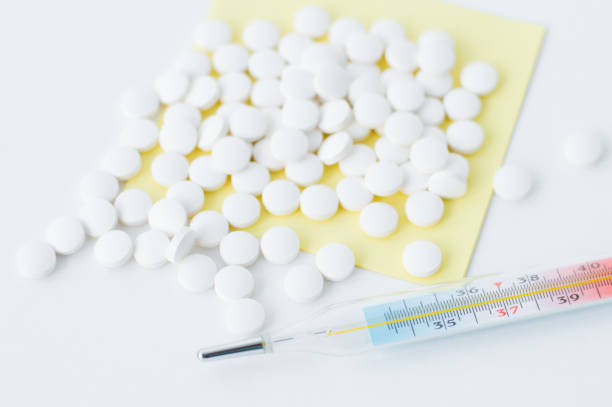 istock Pills scattered on yellow paper and a white table next to a thermometer 1347503986