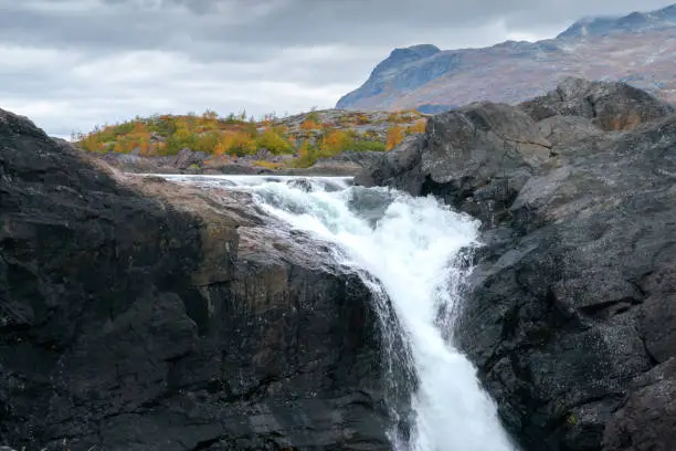 Photo of Closeup, wide, low angle shot of mighty Stuor Muorkkegarttje waterfall on Lulealven river on a cloudy day of arctic autumn. Stora Sjofallet national park, Sweden.