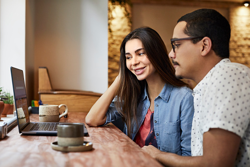 Smiling woman with man looking at laptop in cafe. Male and female friends sitting together at restaurant. They are in casuals.