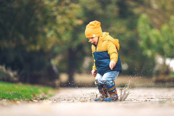 Happy little kid boy jumping on rainy puddle in autumn on nature stock photo
