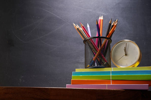 istock pencil holder and alarm clock on top stack of books against blackboard 1347507818