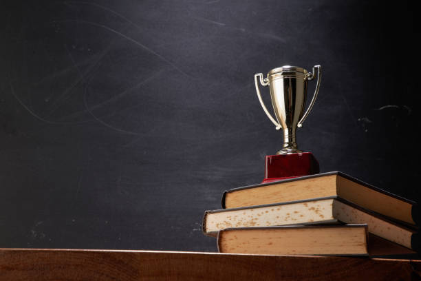 wining trophy on stack of book against blackboard wining trophy on stack of book against blackboard playing sport at university stock pictures, royalty free photos & images