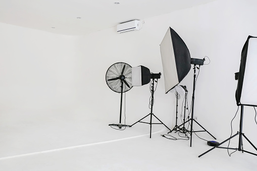 Close-up shot of an empty professional photo studio with flash lights, stands, and fan in a white background wall