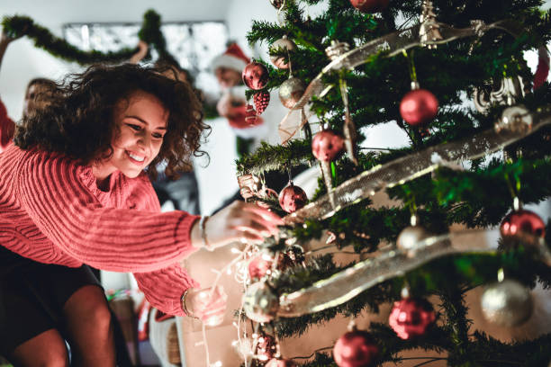 istock Cute Smiling Female Putting Christmas Decorations On Tree While Celebrating With Friends 1347511949