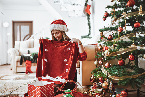 Cute Female Getting Red Reindeer Sweater In Christmas Gift Box Under Tree