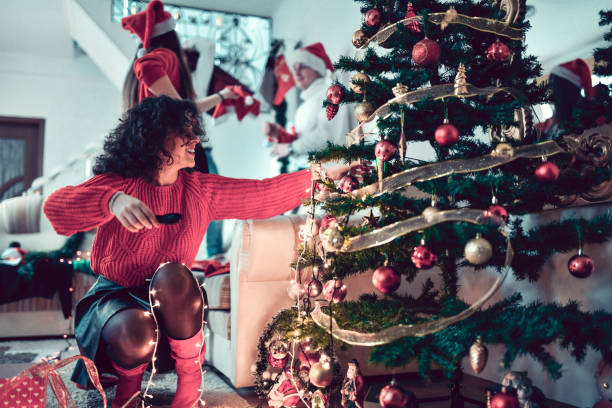 istock Focused Female Adjusting Christmas Decorations On Tree With Friends 1347512761