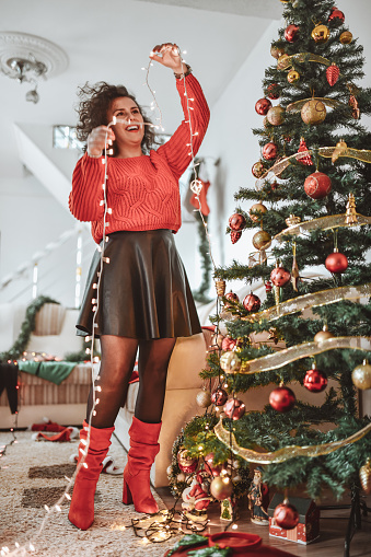 Smiling Female Enjoying Decorating Christmas Tree With Lights At Home
