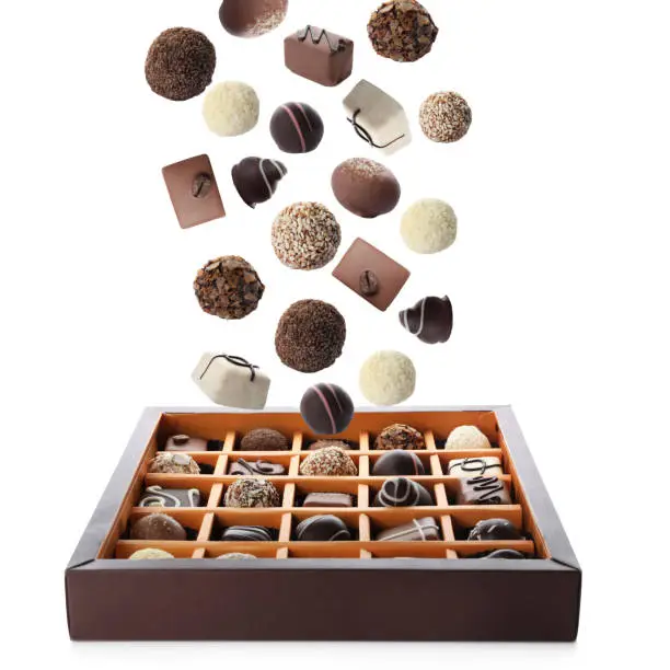 Chocolate candies falling into box on white background