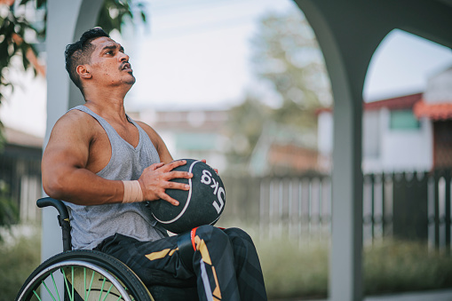 hombre indio asiático discapacitado en silla de ruedas practicando con balón medicinal lanzando en la pared en el patio trasero de su casa en la rutina de la mañana photo