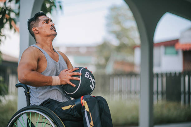 homme indien asiatique handicapé en fauteuil roulant pratiquant avec une balle de médecine jetant sur le mur dans la cour arrière de sa maison dans la routine du matin - un seul homme dâge moyen photos et images de collection