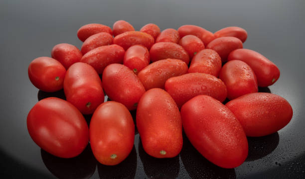 plum tomatoes and cherry tomato composition on a dark glass background. vegan food - plum tomato fotos imagens e fotografias de stock