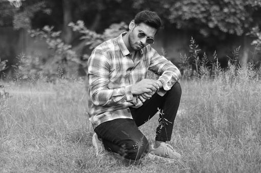 Sitting portrait of young Indian man outdoors in the nature and he watching time in wristwatch.