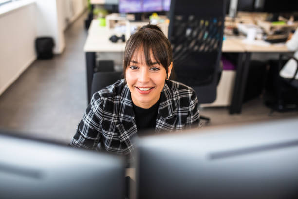 istock A pretty woman smiling behind two computer monitors at the office 1347518878