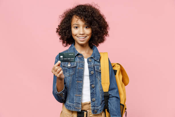 smiling smart little african american kid school girl 12-13 years old in casual denim clothes with backpack hold credit bank card isolated on pastel pink background studio childhood education concept. - 12 13 years fotos imagens e fotografias de stock