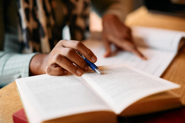 Close-up of African American woman doing some research in a library. Close-up of African American female student learning from books in a library. textbook stock pictures, royalty-free photos & images
