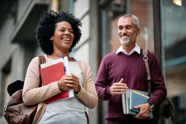 Photo of Happy adult students laughing and having fun in front of university library.