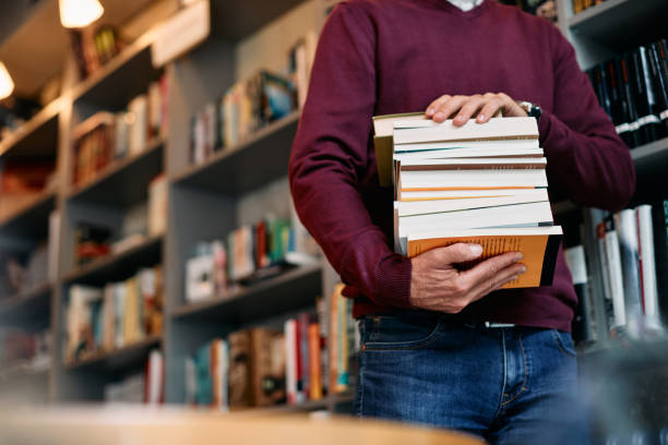 istock Unrecognizable man carrying stack of books in a library. 1347520289
