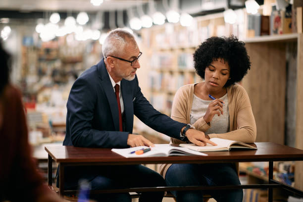istock Mid adult black female student having teacher's assistance while studying in a library. 1347520331