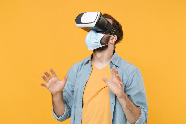 istock Young man in sterile face mask posing isolated on yellow wall background studio portrait. Epidemic pandemic coronavirus 2019-ncov sars covid-19 flu virus concept. Watching in headset spreading hands. 1347520942