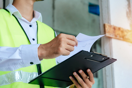 engineer or home inspector in green reflective jacket checking review document and inspecting with clipboard at construction site building interior, construction, contractor and engineering concept