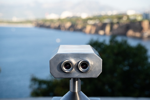rear view closeup of aluminum coin operated binoculars with beautiful sea and mountains landscape panorama in the background