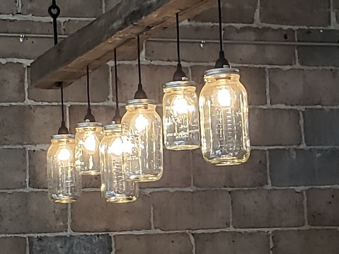 A modern and chic style of chandelier in which individual light bulbs are encased individually in a clear glass sconce hung by steel rods from a large wooden beam.