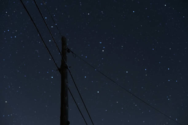Silhouette of an electric utility pole and wires, sky is filled with stars