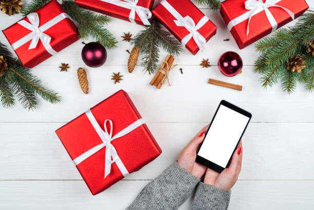 istock Woman holding in hands mobile cellphone with blank touch screen for app presentation, copy space. Christmas decorations. Flat lay, top view. Application mock up template 1347528793