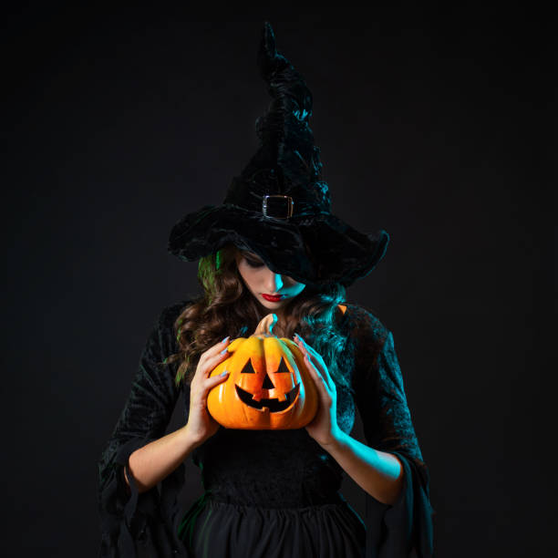 istock beautiful witch in a pointed hat holds a pumpkin with burning eyes, in her hands 1347531155