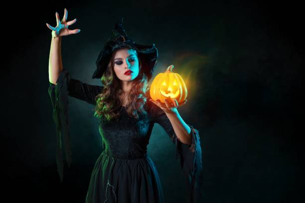 istock beautiful witch with a hat conjures over jack-o-lantern pumpkin. 1347531156
