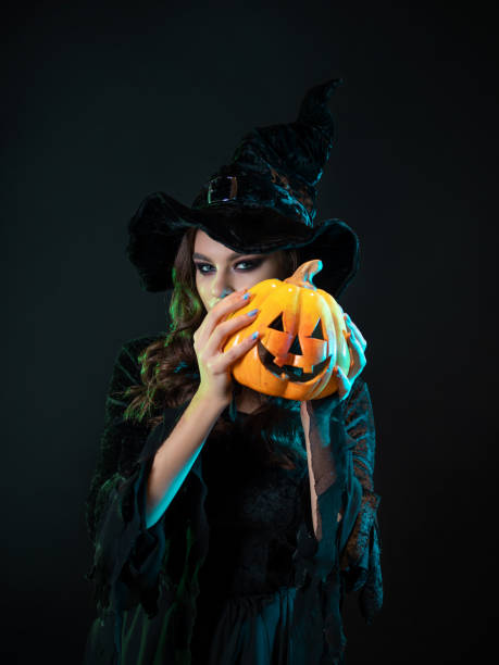 istock beautiful witch in a pointed hat Holding a pumpkin with a laughing face, 1347531161