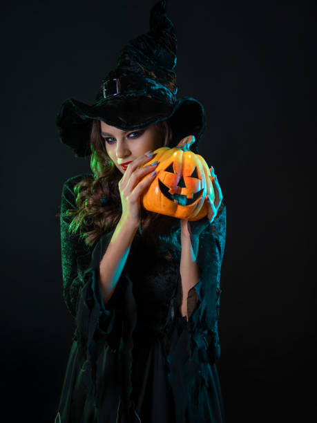 istock tricky beautiful witch in a pointed hat Holding a pumpkin with a laughing face, 1347531169