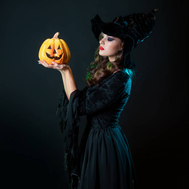 istock beautiful witch in a pointed hat Holding a pumpkin with a laughing face, 1347531700