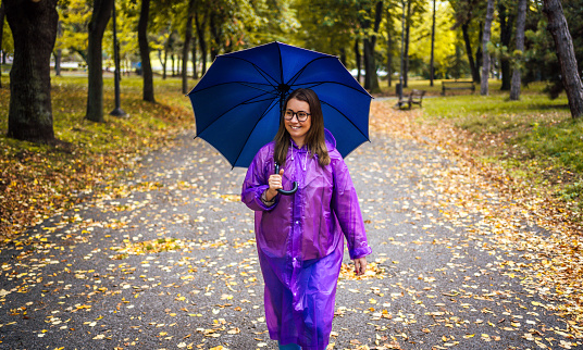 Smiling young woman under blue umbrella outdoors in the rain