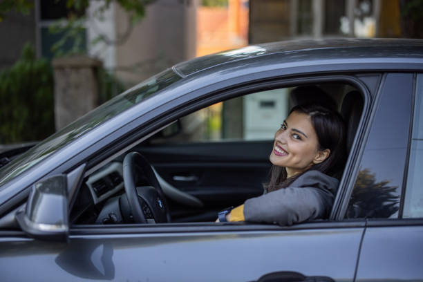 istock Young smiling woman sitting in car with window down and looking at camera 1347537056