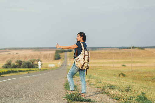 Brunette girl with a backpack catches the car hitchhiking. concept-travel, adventure, freedom.