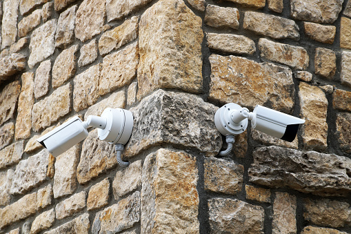 two outdoor surveillance cameras on the corner of an old brick building close-up