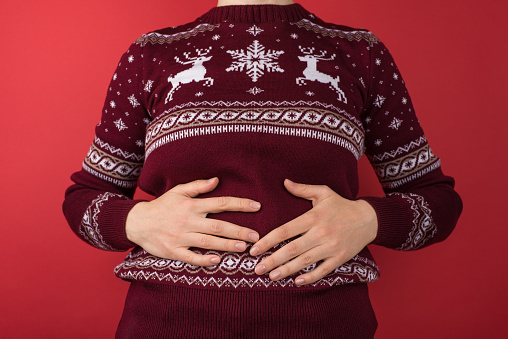 Cropped closeup photo of girl in red and white christmas sweater holding her hurting stomach on isolated red background