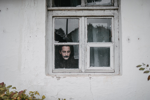 Portrait of a disguised man standing behind a old window