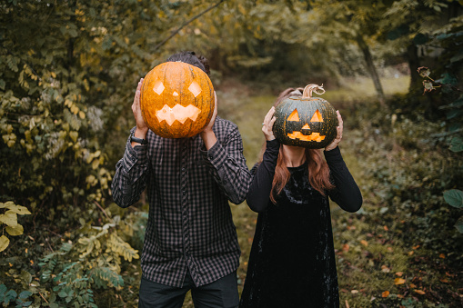 Man and a woman in Halloween costumes holding two carved pumpkins in front of heads. Halloween monsters