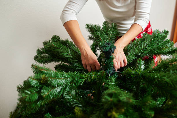 Unrecognizable woman assembling christmas tree Unrecognizable woman assembling artificial christmas tree in her living room wearing christmas pajamas artificial stock pictures, royalty-free photos & images