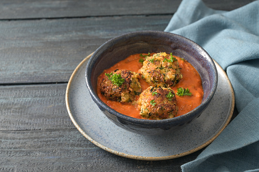 Fried vegetable balls from zucchini and potato in tomato sauce, vegan vegetarian meatball alternative in a blue bowl on a rustic wooden table, copy space, selected focus, narrow depth of field