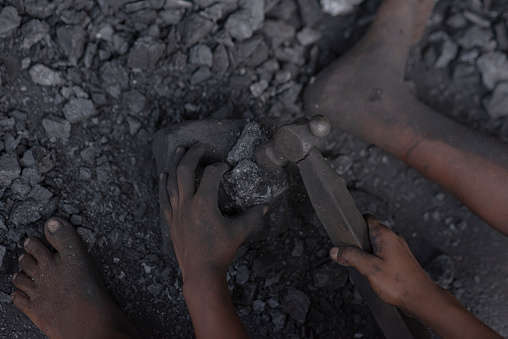 Hard working little boy breaking coal with iron hammer and collecting coals closeup photo