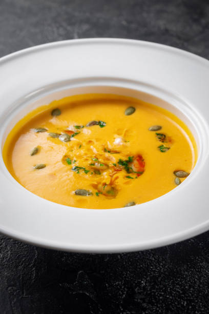 istock Pumpkin cream soup pureed in a white plate on a dark stone table 1347545584