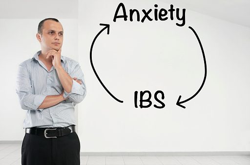 Businessman looking at  “Anxiety and IBS”  text on a transparent screen.