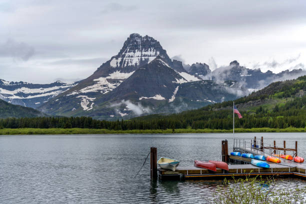 A U.S. Flag flying above a boat launch at Swiftcurrent Lake, with Mt. Wilbur towering at west shore, on a stormy Spring morning. Many Glacier, Glacier National Park, Montana, USA.