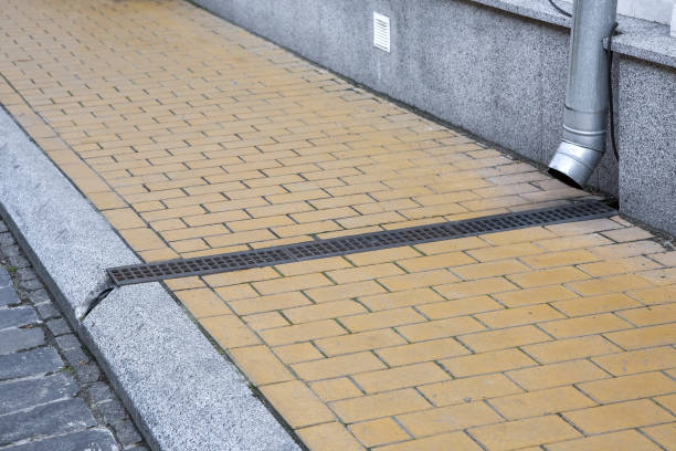 istock facade of building with granite stone cladding with storm pipe into drainage canal with iron grating on pedestrian sidewalk made of stone tiles and curb by road, improvement of old city, nobody. 1347549483